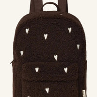 A dark brown teddy fleece backpack with a pattern of small white embroidered hearts, featuring a front pocket and dual shoulder straps, shown against a plain white background.