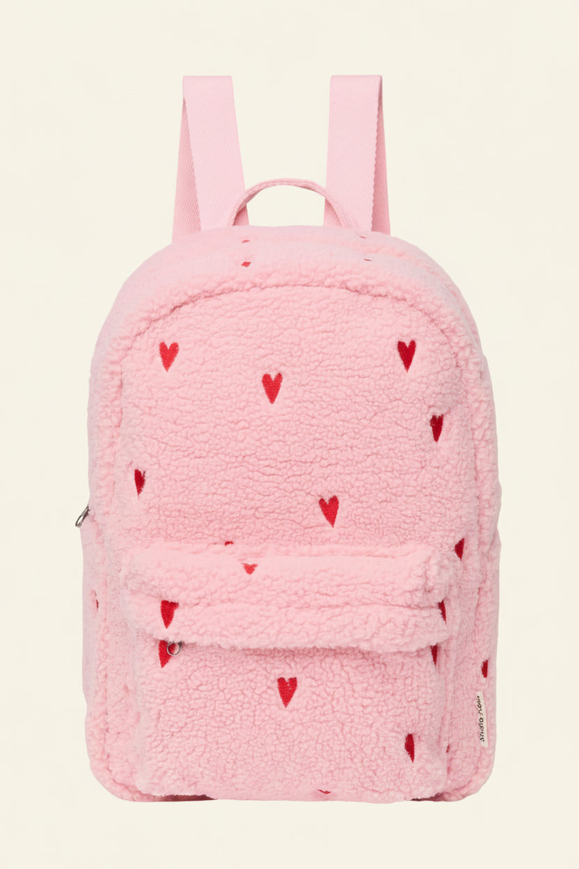 A pink teddy fleece backpack with small red heart details and a front flap pocket, shown on a plain white background.