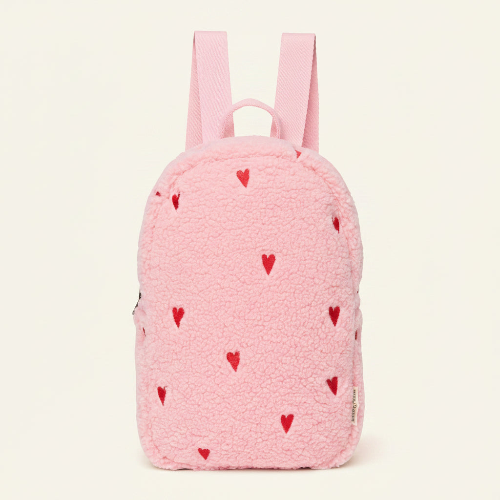A pink fleece backpack with small red heart patterns, featuring dual shoulder straps and a top carry handle, shown against a plain white background.
